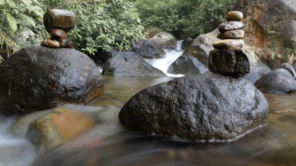Calm river with rock balancing in Pangalengan, Indonesia, surrounded by lush greenery.