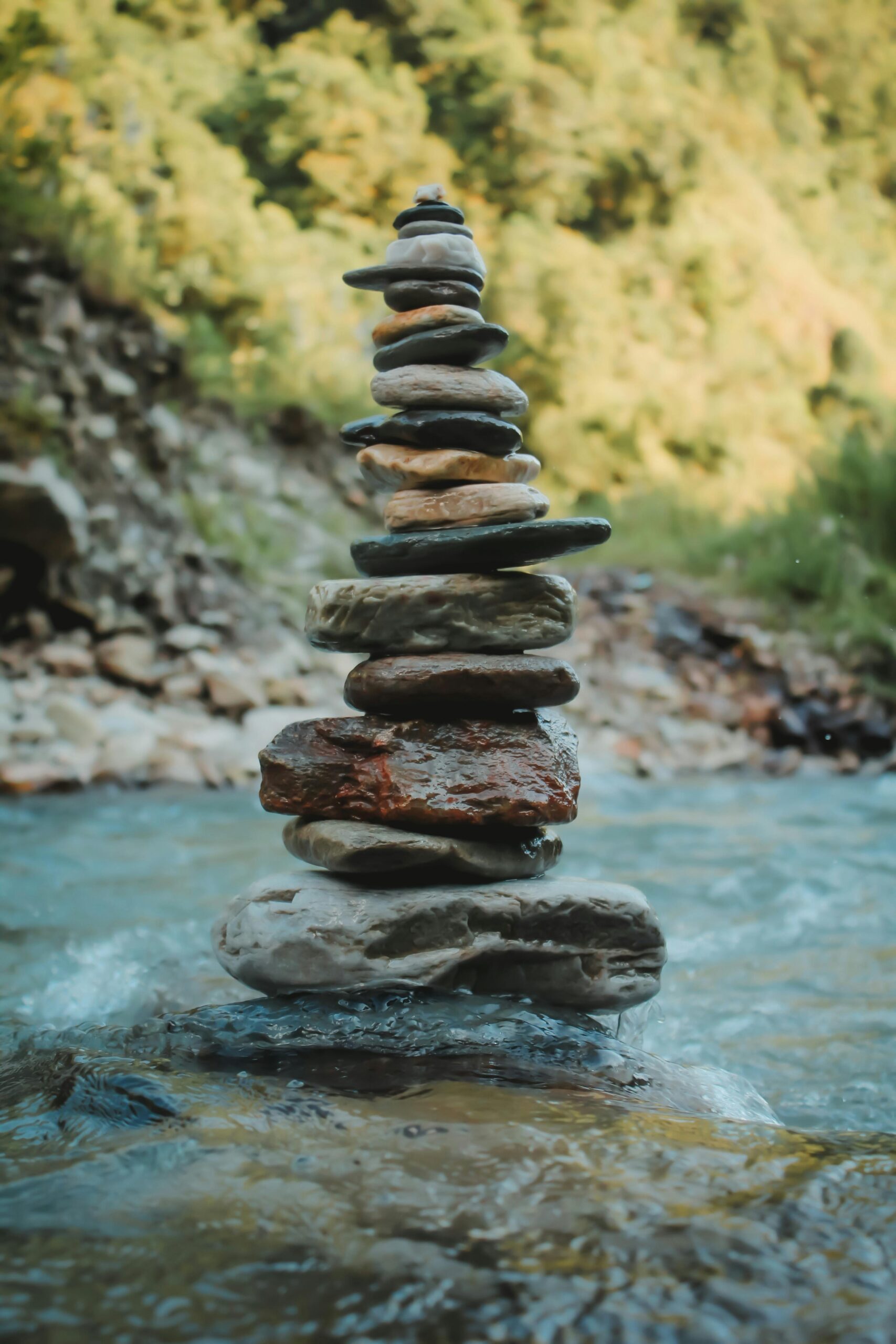 A balanced stack of stones by a flowing river amidst lush greenery.